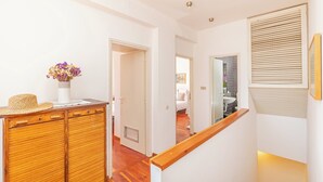 A hallway with a wooden cabinet, a vase with flowers, and a staircase with a wooden handrail.