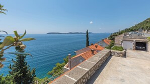 A coastal property with a stone retaining wall, a red-tiled roof, and a view of the sea.