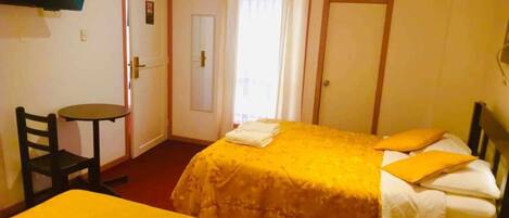 A hotel room with two beds, a TV mounted on the wall, a small table, and a door leading to a balcony.