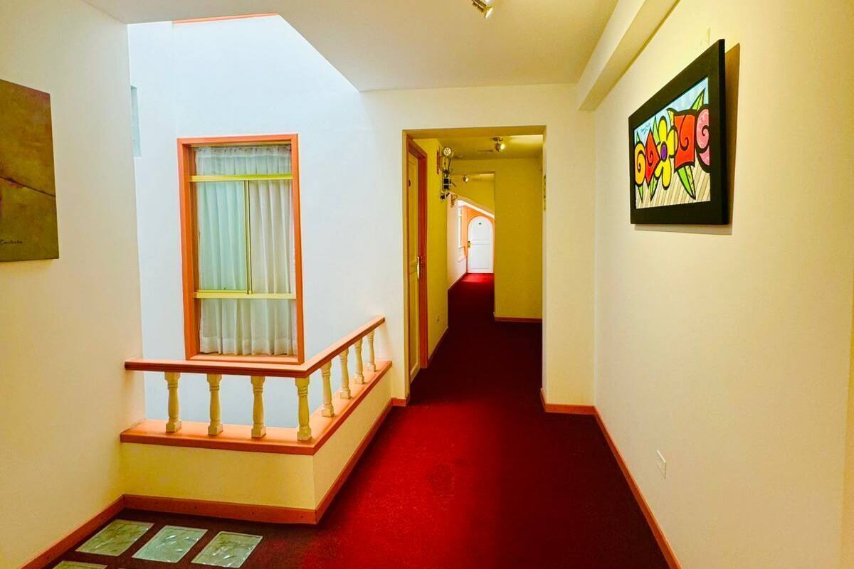 Un pasillo con alfombra roja, una escalera con barandilla de madera y una obra de arte enmarcada en la pared.