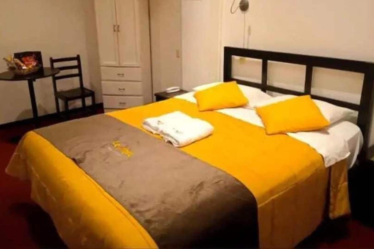 Una cama con una colcha amarilla y marrón, dos almohadas y una toalla doblada.