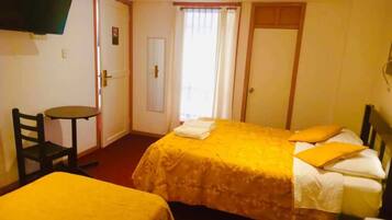 Habitación de hotel con dos camas, televisión montada en la pared, una mesita y puerta que da a un balcón.