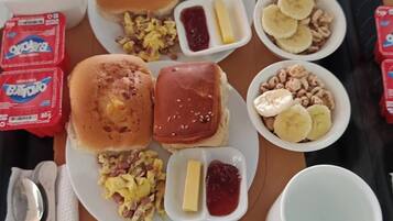 Bandeja con alimentos para el desayuno, incluyendo panqueques, huevos revueltos y un muffin, junto con salsas y una taza.