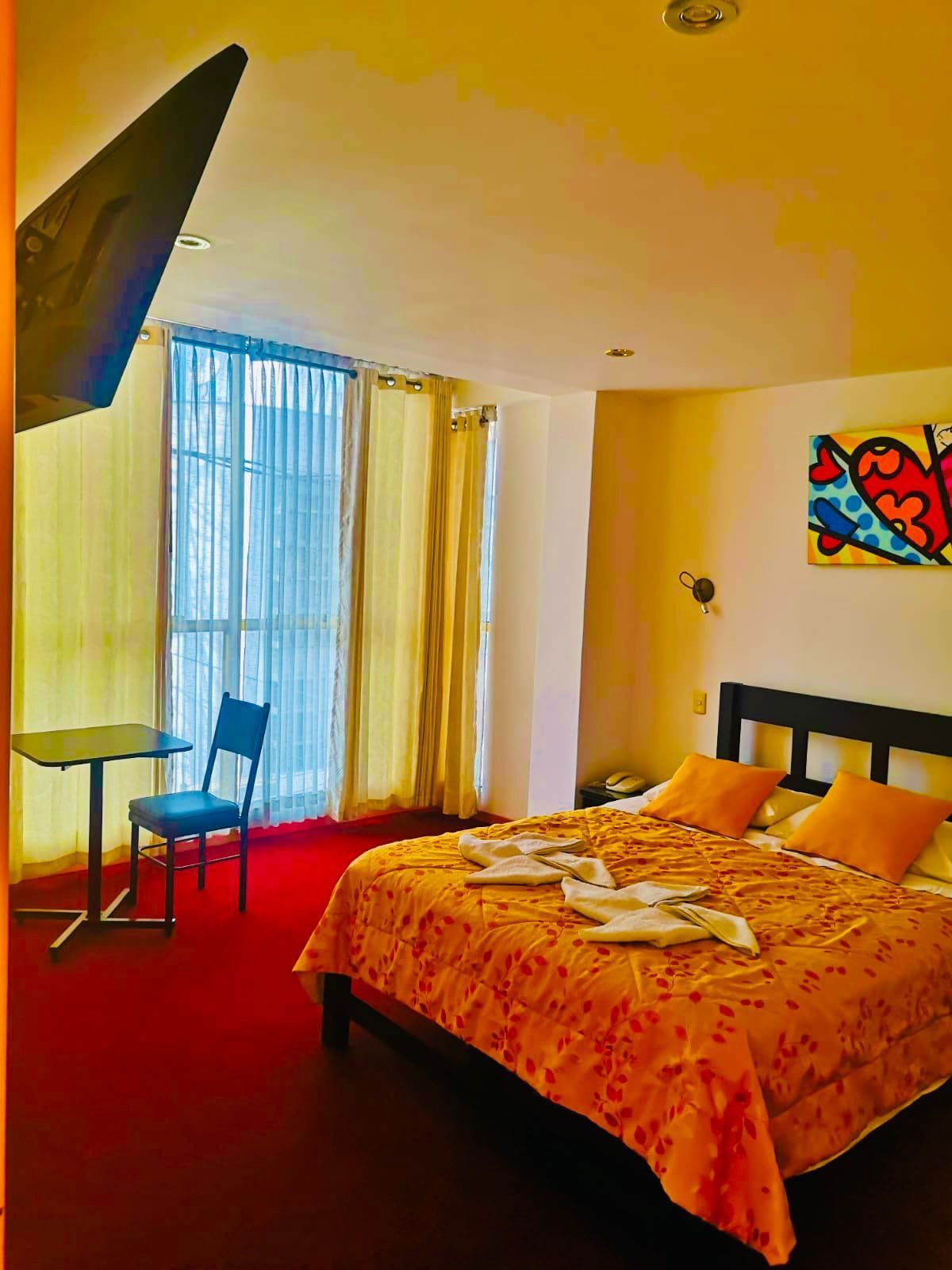 Une chambre d’hôtel avec un lit, une chaise, une table et une fenêtre avec des rideaux.
