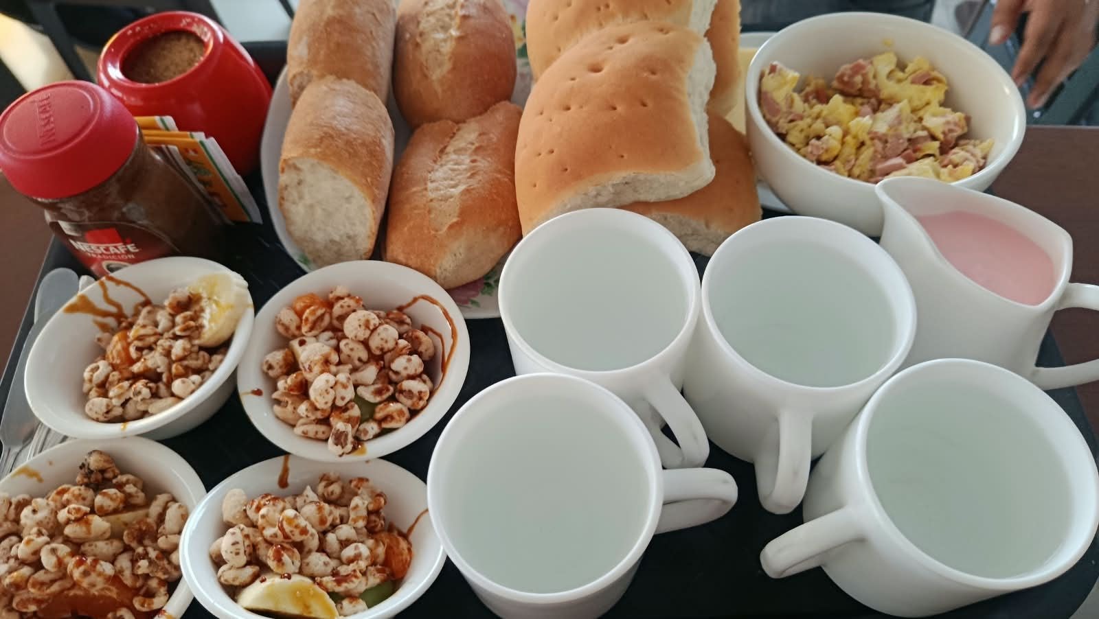 A table with various food items and cups, including bread, cereal, and a jar of sauce.