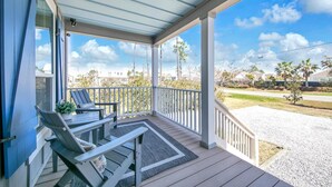 A covered porch with two lounge chairs and a small table, overlooking a residential area with houses and palm trees. - The Claddagh Cottage (Santa Rosa Beach)