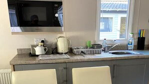 A compact kitchen with a microwave, kettle, and sink. There is a dining table with chairs and a small potted plant.