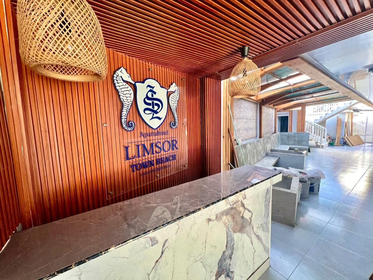 A reception area with a wooden wall, a marble counter, and a sign for 'Aparthotel LIMSOR TOWN BEACH'.