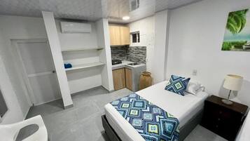 Een compacte hotelkamer met een bed, een klein kitchenette, een badkamer en een zithoek.