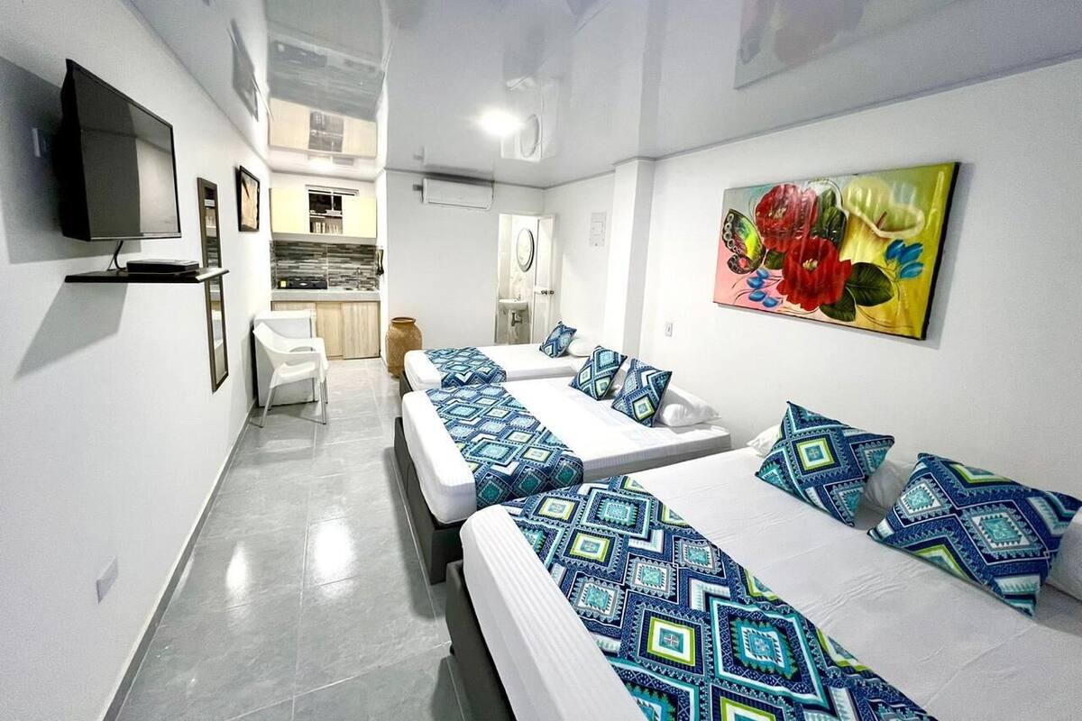 A hotel room with two beds, a TV, a painting, and a kitchenette in the background.