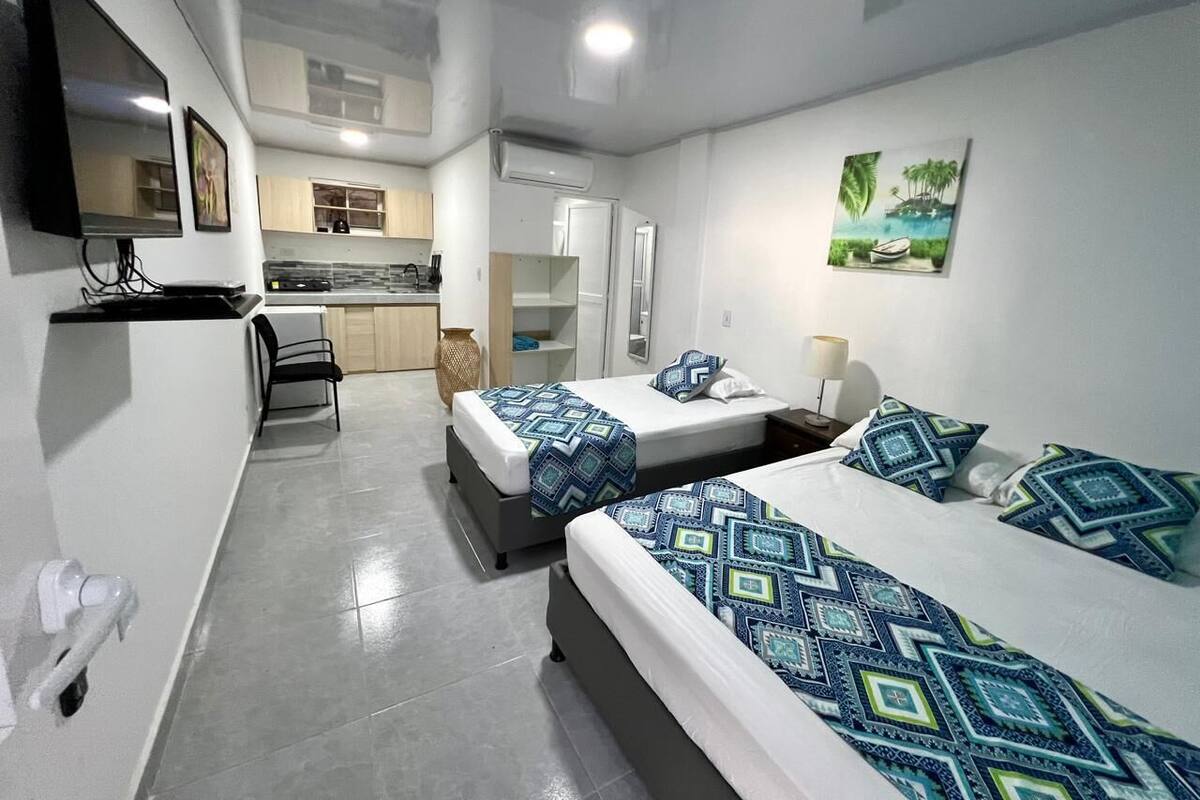 A hotel room with two beds, a TV, a kitchen area, and a painting on the wall.