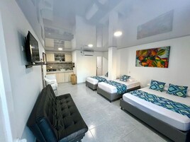 Una habitación de hotel moderna con sofá, dos camas con ropa de cama estampada, una zona de cocina y un ventanal grande.