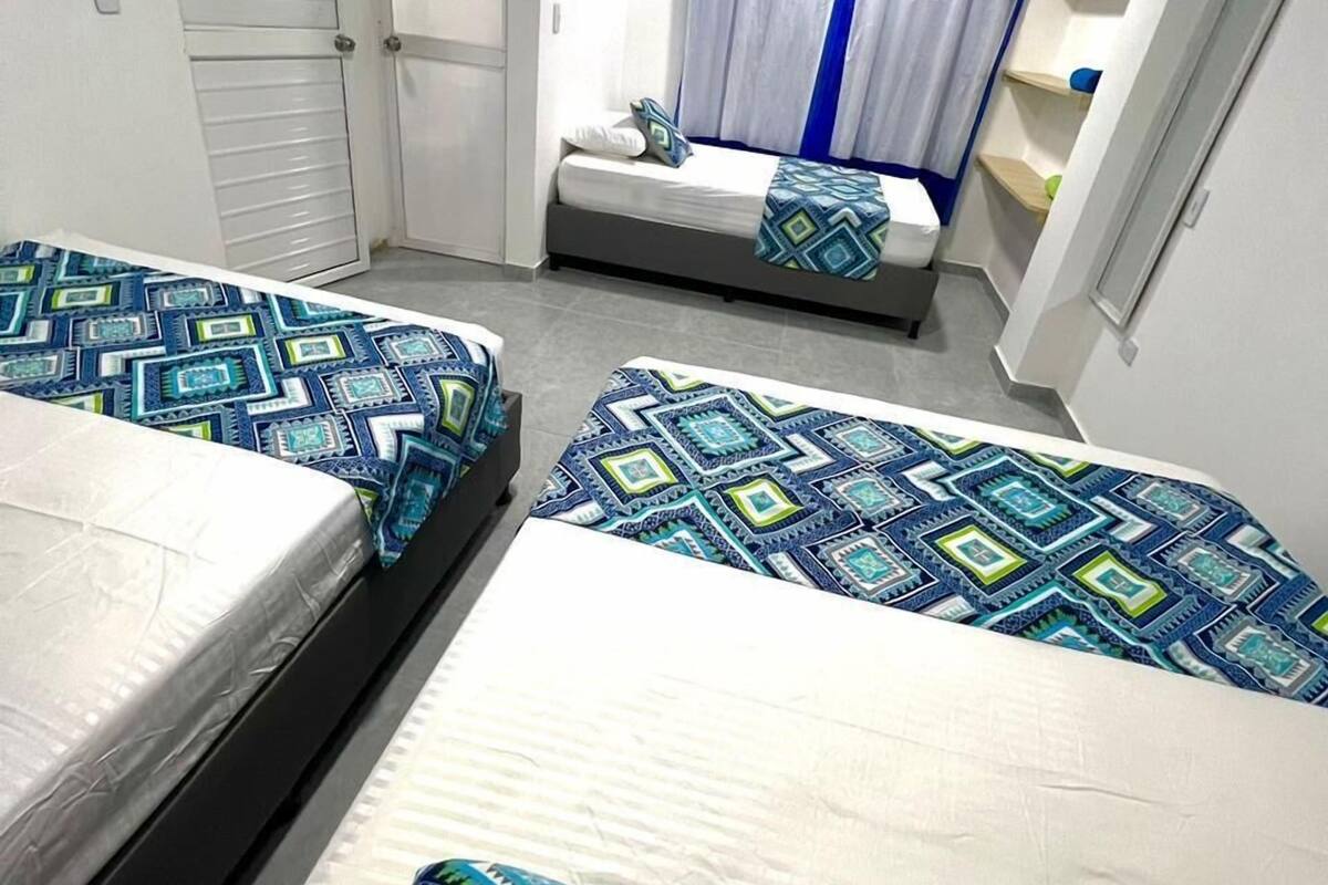 A bedroom with two beds, a window with blue curtains, and a bedside table.