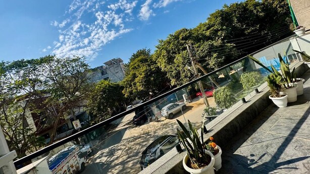 A balcony with potted plants, a clear sky, and a view of the street below. - Luxe 8 Stayz  (Gurugram)