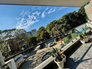 A balcony with potted plants, a clear sky, and a view of the street below. - Luxe 8 Stayz (Gurugram)