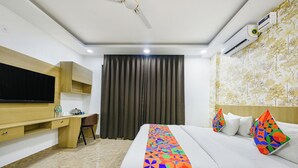 A hotel room with a bed, a desk with a chair, a television, and an air conditioning unit. - Luxe 8 Stayz  (Gurugram)