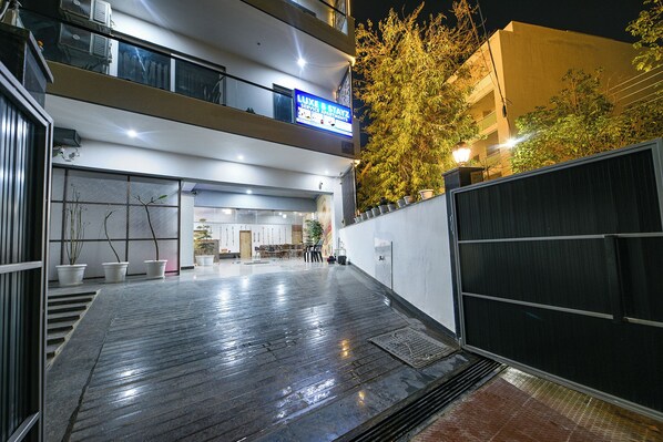 A hotel entrance with a ramp leading to the lobby, a sign for 'Luxe 8 Stayz Service Apartments', and a gated area with potted plants. - Luxe 8 Stayz (Gurugram)