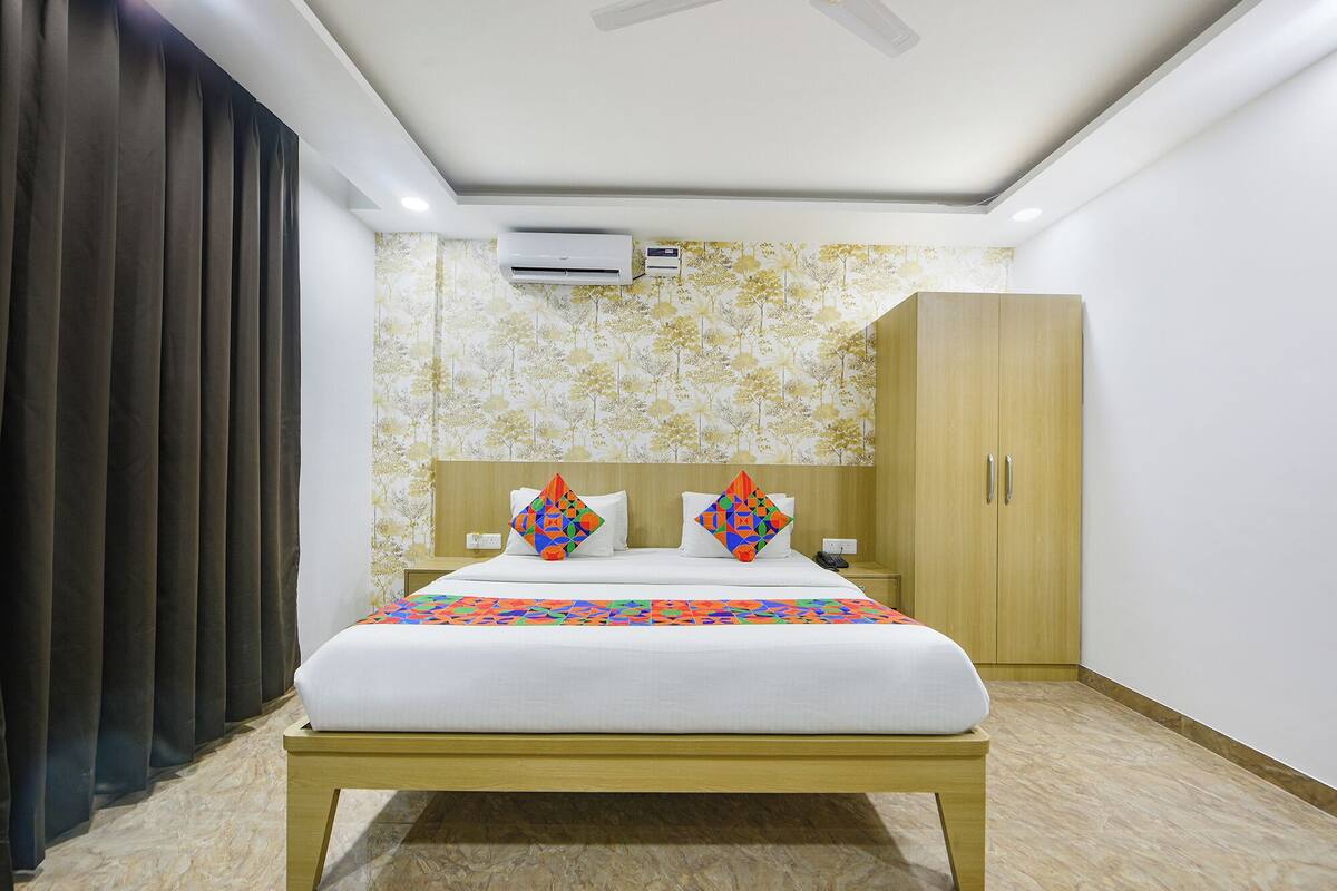 A hotel room with a bed, a wardrobe, an air conditioning unit, and a patterned wallpaper.