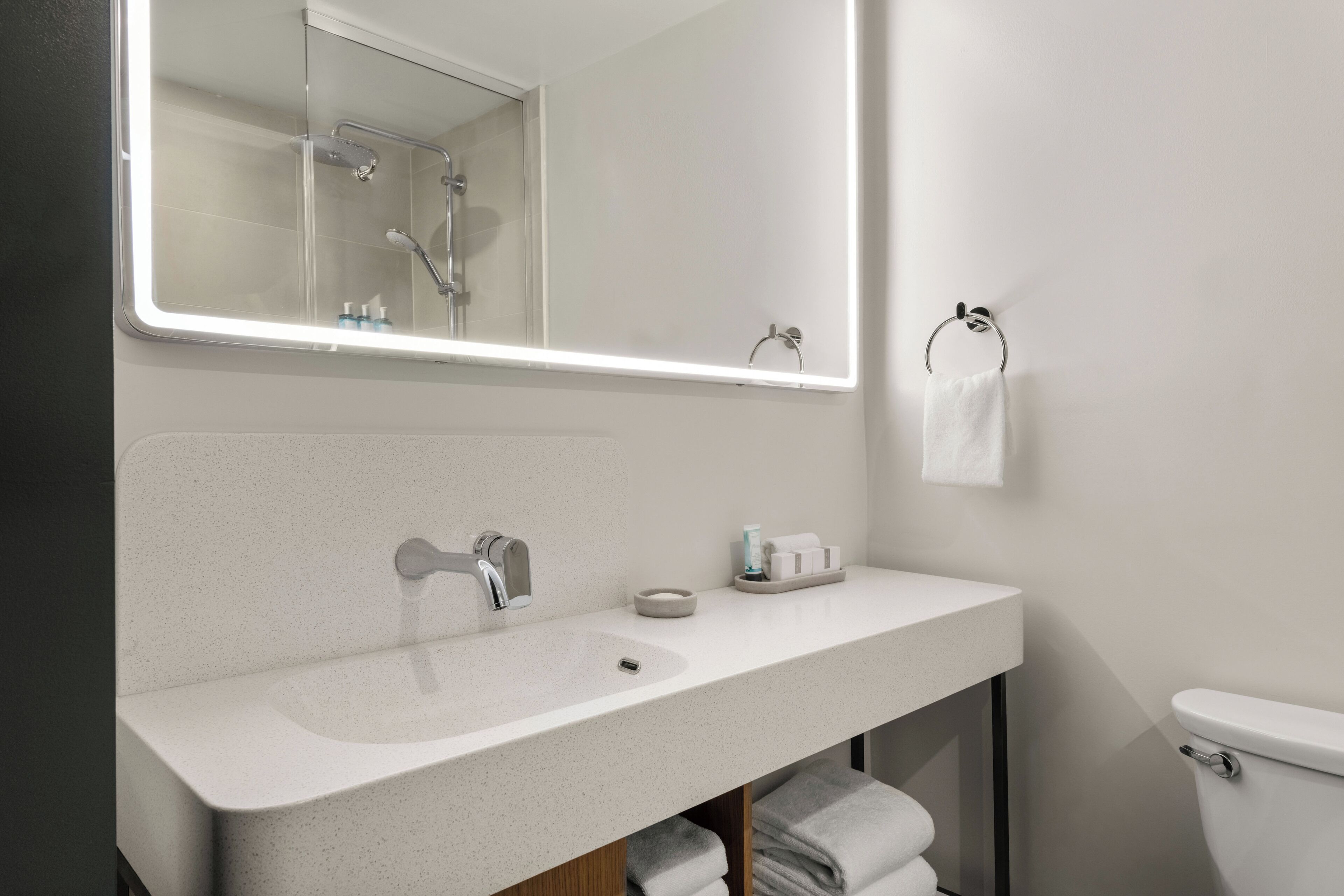A modern bathroom with a white sink, a mirror, a towel rack, and a toilet.