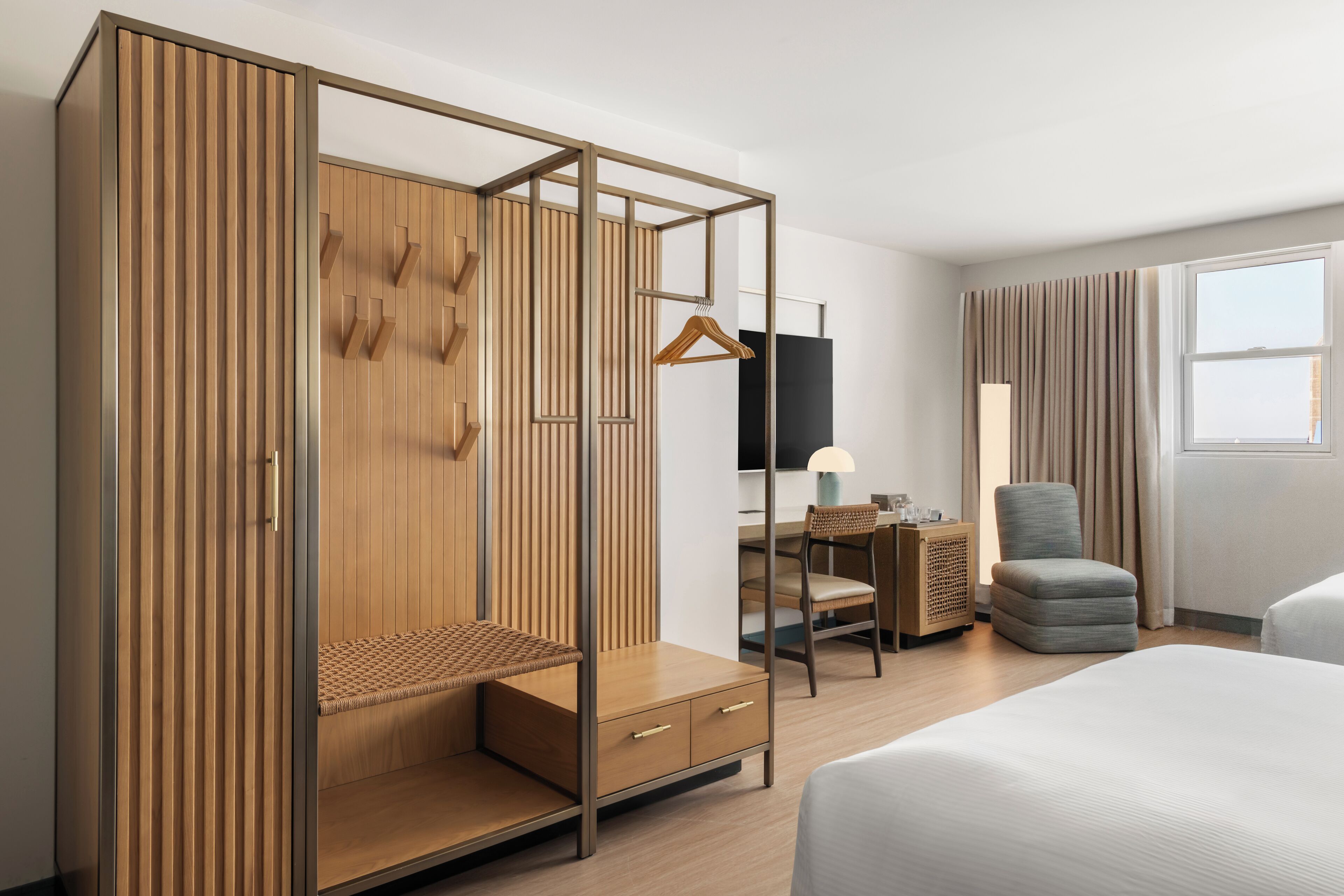Una habitación de hotel moderna con un armario de madera, un escritorio con lámpara, una silla y una cama.
