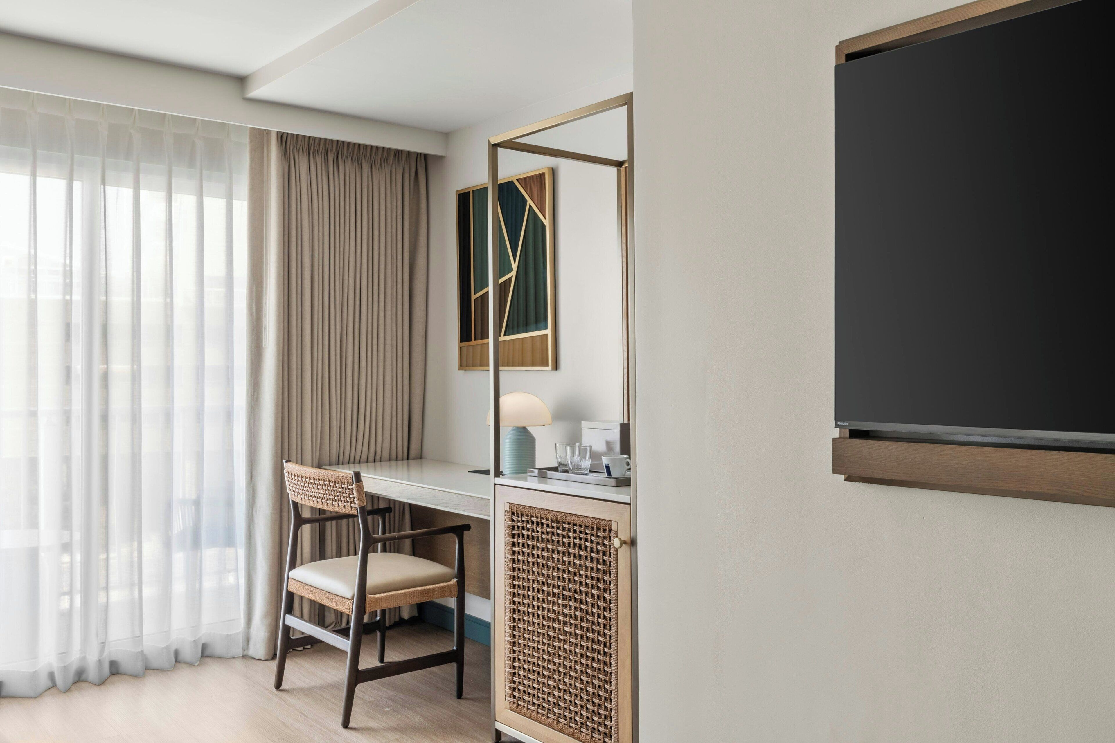A hotel room with a desk, chair, and a large mirror.