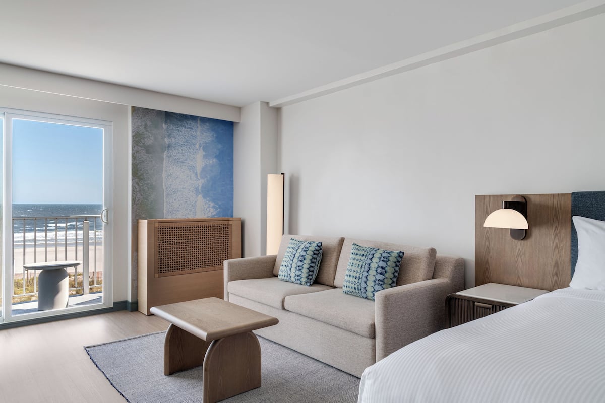 A hotel room with a large window, a sofa, a bedside table, and a bed.