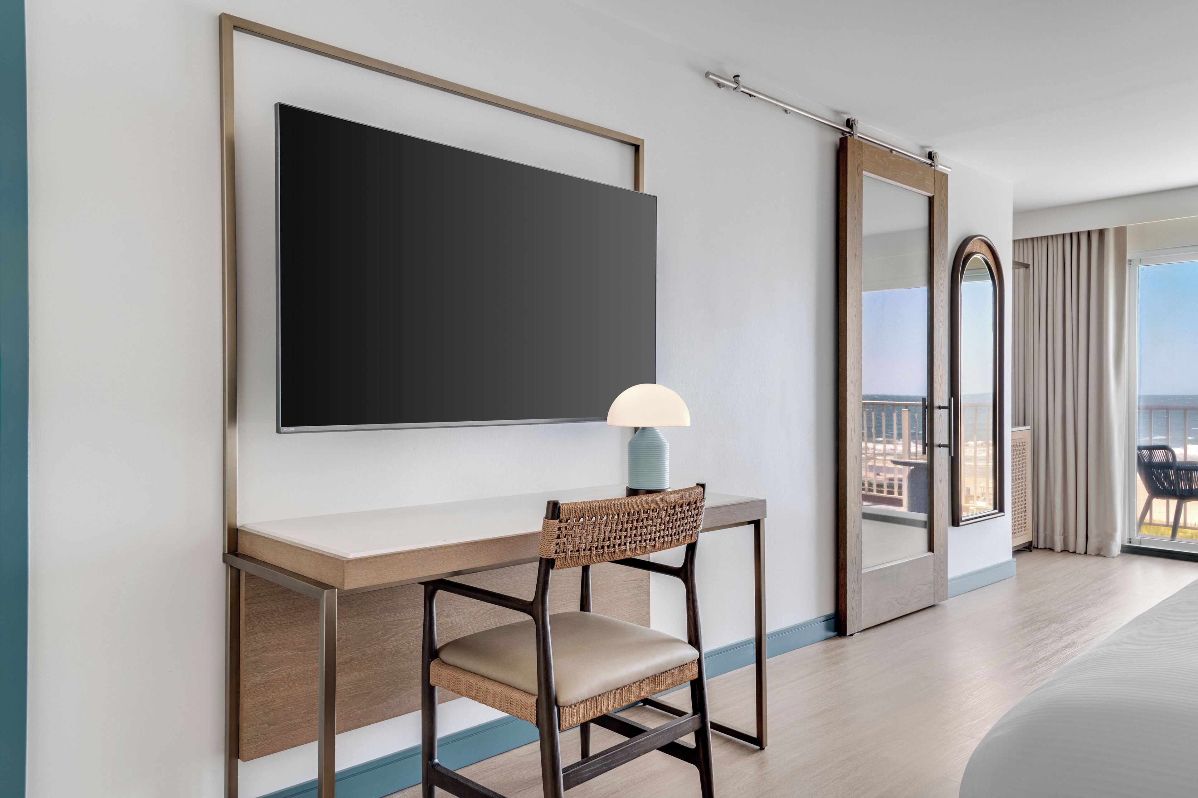 A modern hotel room with a desk, chair, and a large mirror.