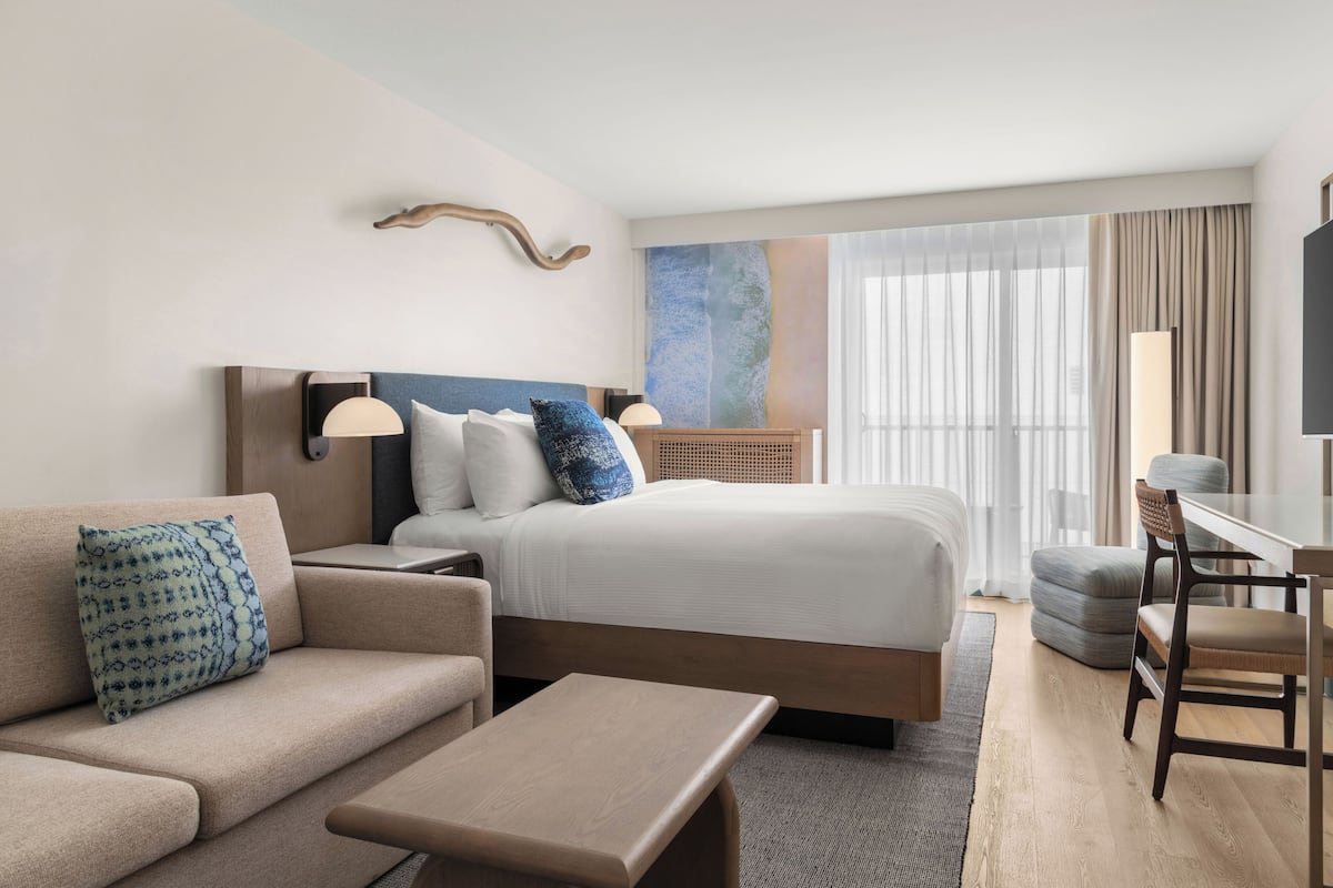 A modern hotel room with a large bed, a sofa, a desk, and a TV.
