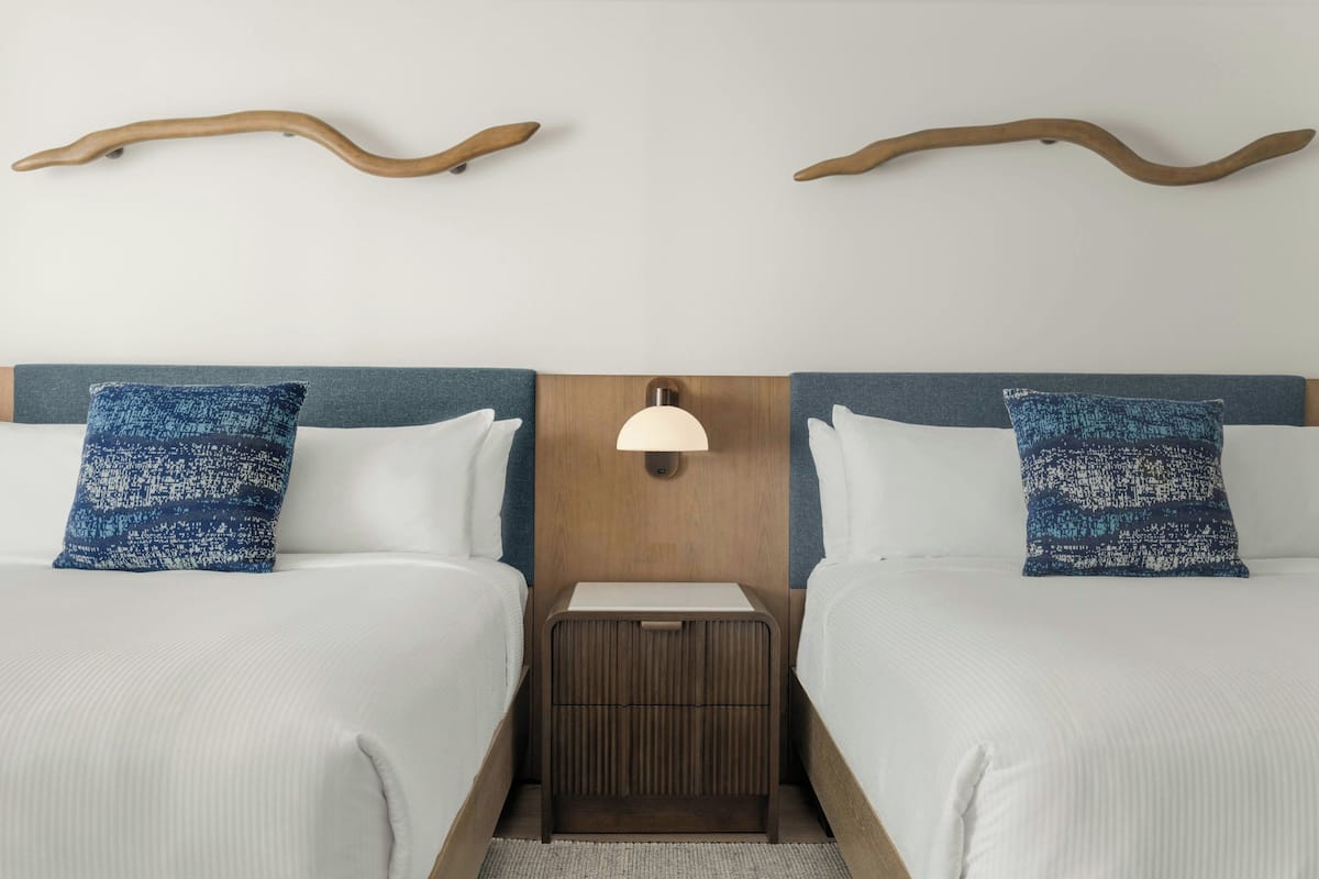 A hotel room with two beds, a nightstand with a lamp, and wooden wall decor.
