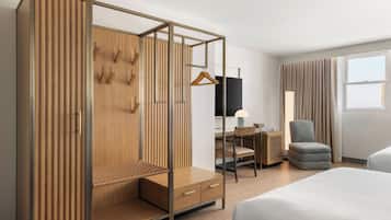 A hotel room with a large bed, a wardrobe with a hanging rack, a desk with a chair, and a lamp.