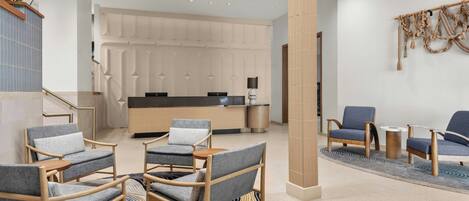 A modern lobby with seating areas, a reception desk, and a staircase.