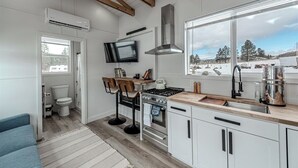 A modern kitchen with white cabinetry, a gas stove, a stainless steel range hood, and a large window offering a view of a snowy landscape.