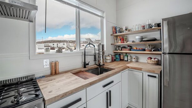 A modern kitchen with white cabinets, a stainless steel refrigerator, and a window with a city view.