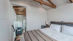 A bedroom with a large bed, a bedside table, a lamp, and a view of a hallway.