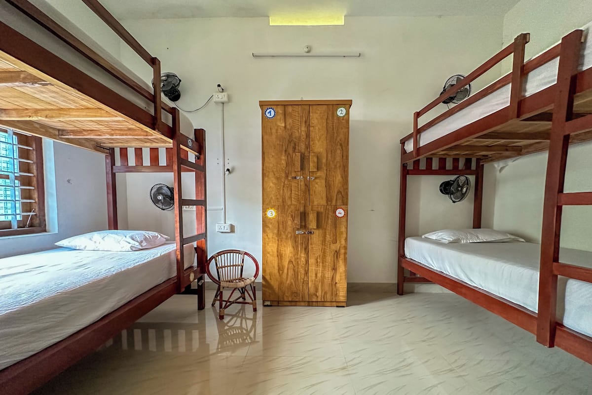 A room with bunk beds, a wooden door, a chair, and a fan.