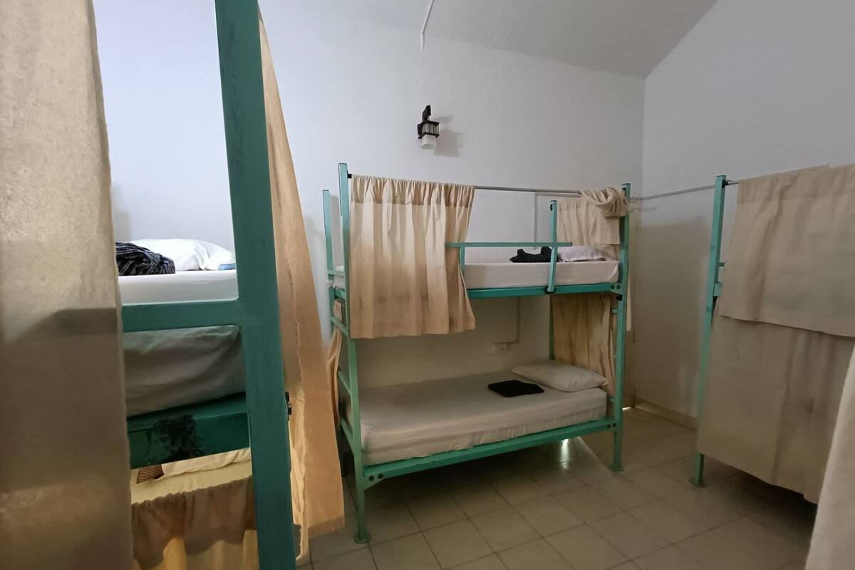 A dormitory room with bunk beds, a small table, and a wall-mounted light fixture.