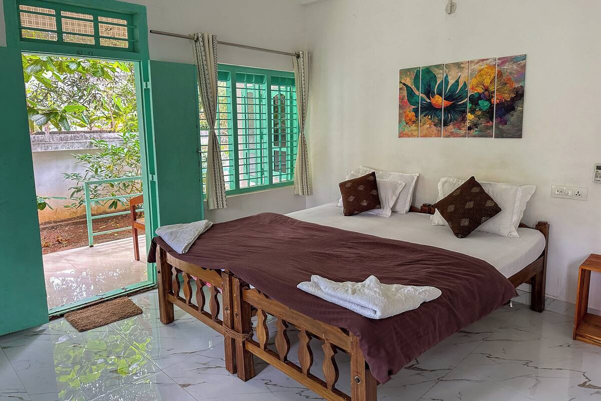 A bedroom with a bed, a painting, and a view of greenery outside.