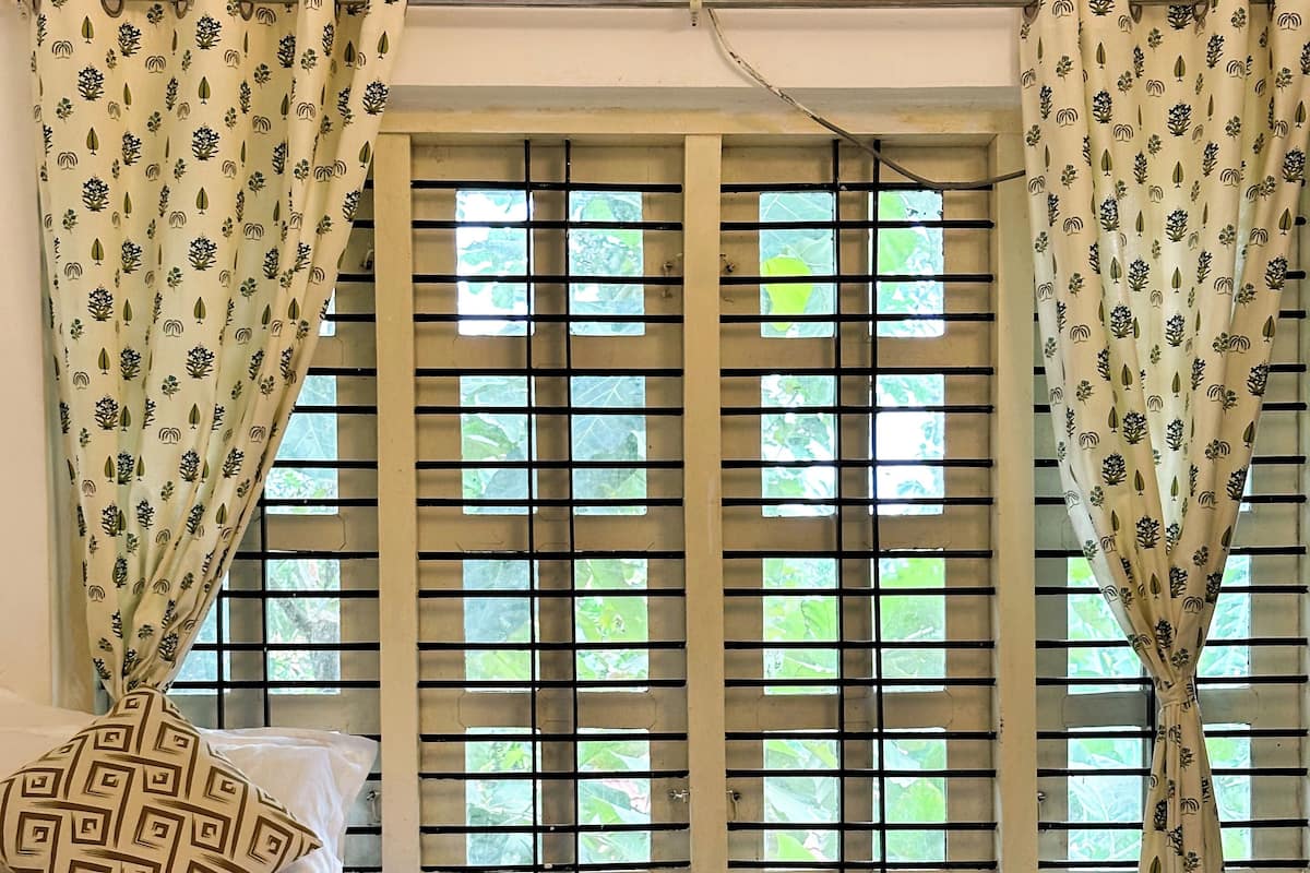A bedroom with a bed, a window with blinds, and a patterned curtain.
