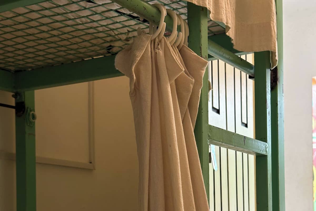 A bunk bed with a green frame and a beige curtain.
