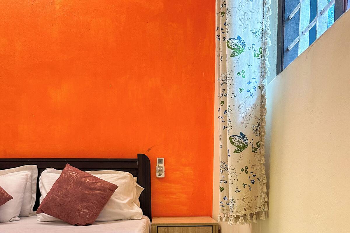 A room with a bed, a bedside table, a telephone, and a window with curtains.