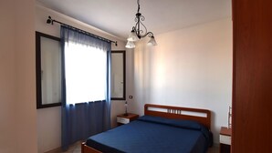 Un dormitorio con una cama, una mesita de noche, una lámpara, una ventana con cortinas y una lámpara colgante.