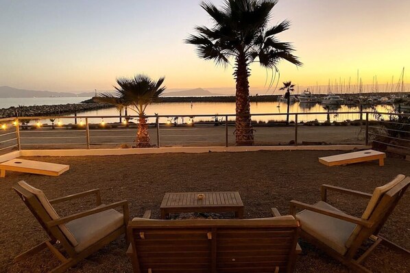 An outdoor seating area with wooden chairs and a table, overlooking a marina with boats and a calm sea.