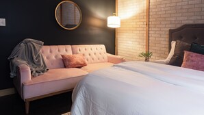 A bedroom with a pink sofa, a bed with white bedding, a round mirror, and a brick wall. - Abe's Hideaway - Arcade, Hot Tub, Home Theater - Quiet upscale neighborhood (Springfield)