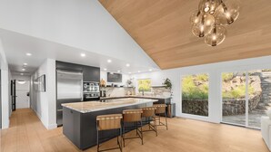 Una cucina moderna con isola centrale, sgabelli da bar e un'ampia finestra che si affaccia su un giardino.