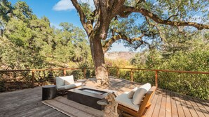 Un patio in legno con un braciere, posti a sedere all'aperto e un grande albero che offre ombra.