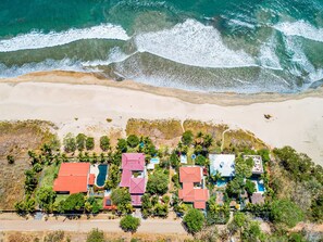 An aerial view of a coastal property with multiple buildings, a swimming pool, and a beach.