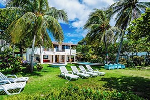 A two-story house with a swimming pool, surrounded by palm trees and a well-maintained lawn. - Host Large Groups in these Stunning Neighboring Beachfront Villas (Playa Grande)