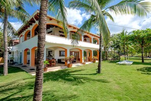 A two-story building with a white exterior and orange accents, surrounded by palm trees and a well-maintained lawn.