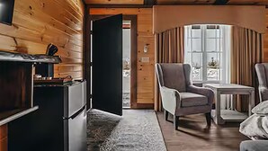 Interior acollidor d'una cabana amb una llar de foc, un sofà còmode i una taula a prop d'una finestra.