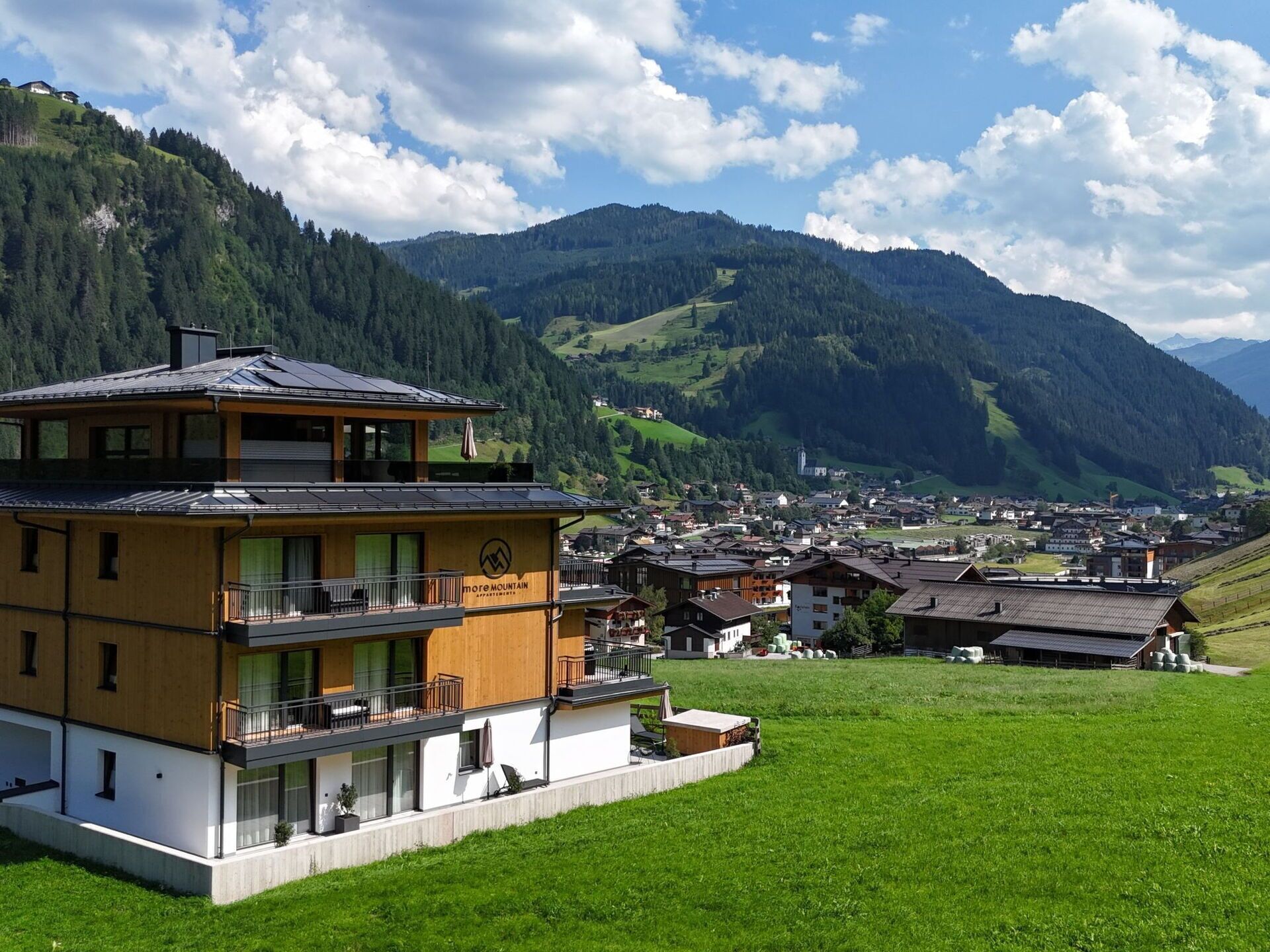 Un bâtiment moderne à deux étages, doté d’un balcon et offrant une vue sur un village et des montagnes en arrière-plan.